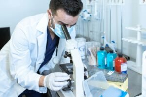 Scientist in a lab coat examining samples using a microscope.