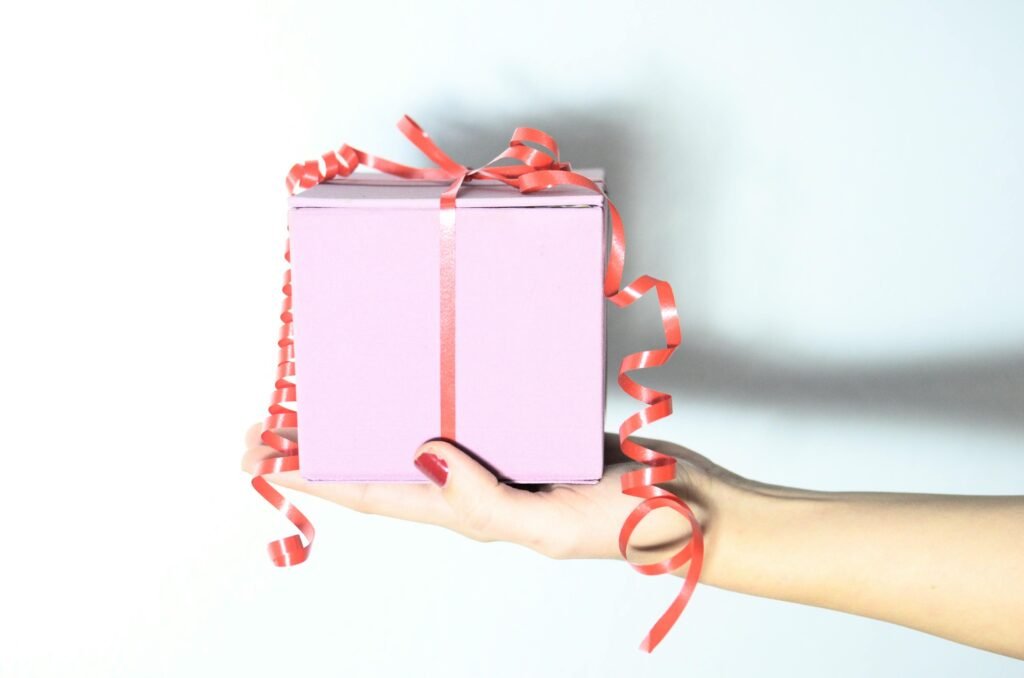 Unrecognizable female with pink present box tied with red ribbon in hand on white background with shadow in light room